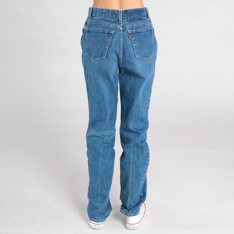 May include: A pair of blue denim jeans with a high waist and straight legs. The jeans have a classic five-pocket design and a button fly.