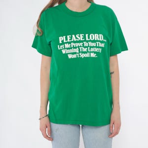K&ouml;nnte beinhalten: Ein gr&uuml;nes T-Shirt mit dem Text "PLEASE LORD... Let Me Prove To You That Winning The Lottery Won't Spoil Me." in Wei&szlig;. Das Shirt hat kurze &Auml;rmel und einen Rundhalsausschnitt.
