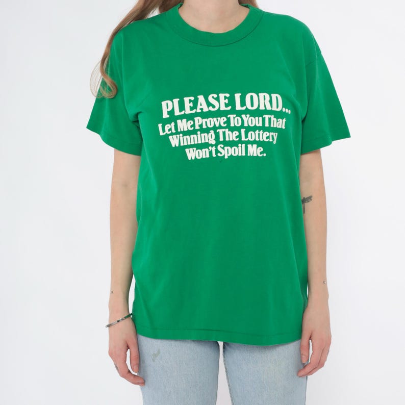 K&ouml;nnte beinhalten: Ein gr&uuml;nes T-Shirt mit dem Text "PLEASE LORD... Let Me Prove To You That Winning The Lottery Won't Spoil Me." in Wei&szlig;. Das Shirt hat kurze &Auml;rmel und einen Rundhalsausschnitt.