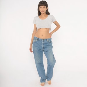 Peut inclure: Un haut court gris clair et un jean en denim bleu clair. Le haut &agrave; manches courtes a une encolure arrondie. Le jean est de couleur claire avec une coupe d&eacute;contract&eacute;e. Le mod&egrave;le se tient devant un fond blanc.