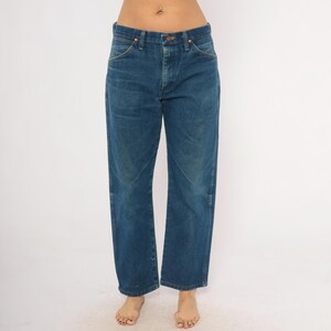 May include: Blue denim jeans with a classic straight leg fit. The jeans have a button and zipper closure, with front and back pockets. The denim has a slightly faded appearance, suggesting wear. The jeans are a medium wash blue.