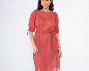 Könnte beinhalten: Ein rotes Midikleid mit quadratischem Ausschnitt und Puffärmeln. Das Kleid hat einen Gürtel an der Taille und einen leicht gerafften Rock.