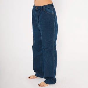 May include: Dark blue denim jeans with a classic five-pocket design. The jeans have a straight leg cut and a button and zipper closure. The denim appears to be a medium weight, suitable for everyday wear. The jeans are shown against a plain white background.