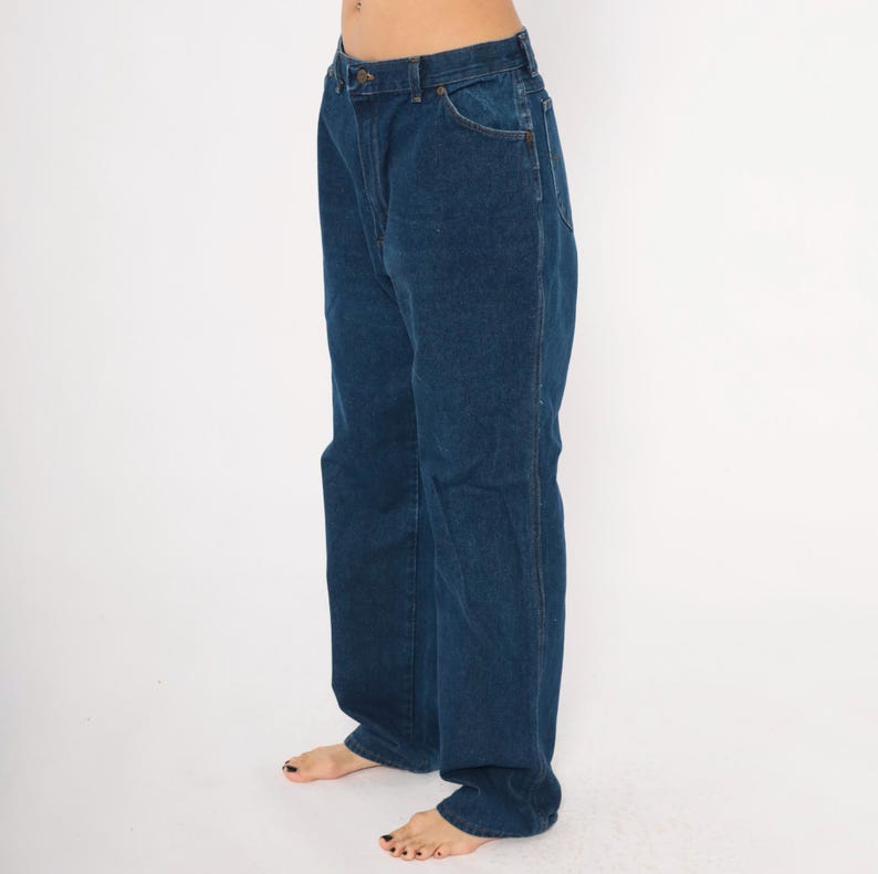 May include: Dark blue denim jeans with a classic five-pocket design. The jeans have a straight leg cut and a button and zipper closure. The denim appears to be a medium weight, suitable for everyday wear. The jeans are shown against a plain white background.
