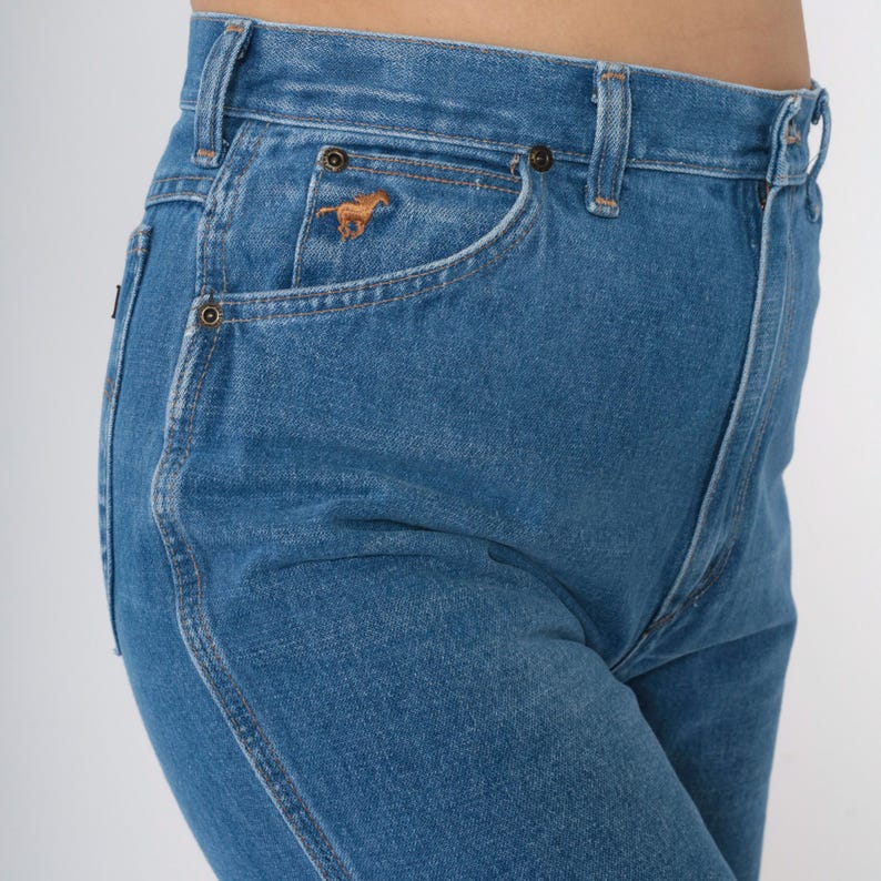 Op de afbeelding: Een paar blauwe denim jeans met hoge taille en een klein bruin paardenlogo op de rechterzak.
