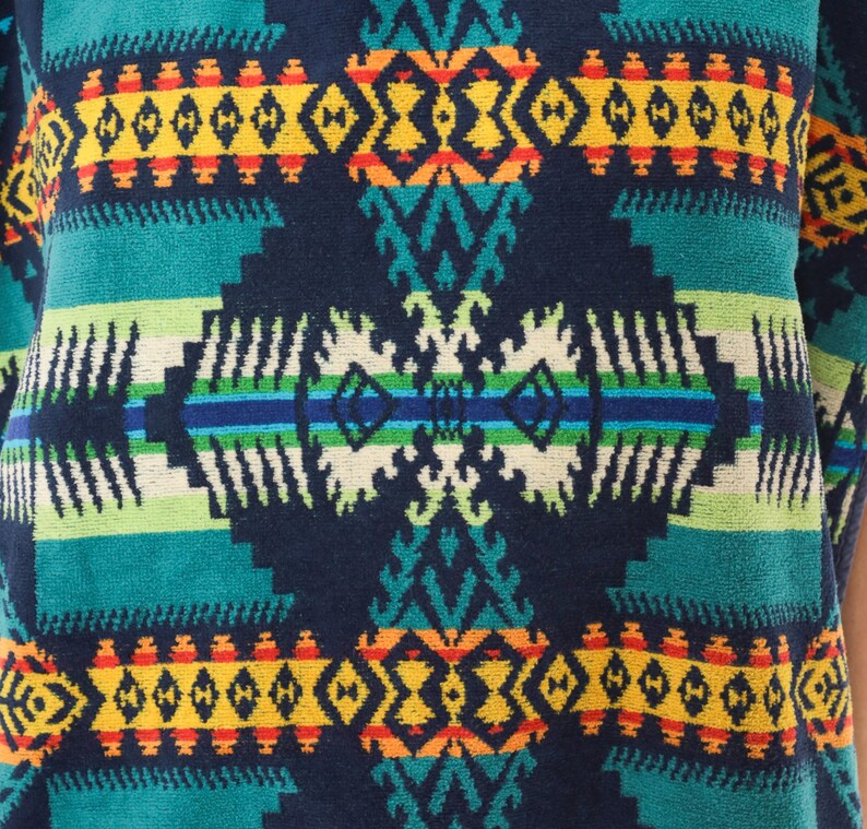 May include: A textile fabric featuring a repeating geometric pattern in dark blue, teal, yellow, orange, and white. The design consists of horizontal bands and symmetrical diamond-shaped motifs with intricate jagged edges and linear details.