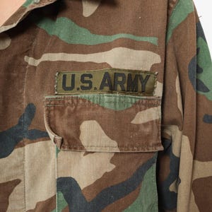 May include: A camouflage green, brown, and black military jacket with a patch that reads "U.S. ARMY" on the left chest.