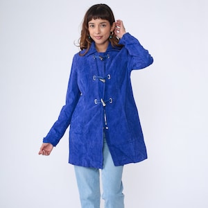 May include: A royal blue suede coat with a long, fitted silhouette and a toggle closure. The coat has a collar and long sleeves.