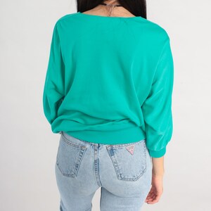 May include: A teal blue long-sleeved sweater with a ribbed neckline and cuffs. The sweater is made of a soft, comfortable fabric and has a relaxed fit.