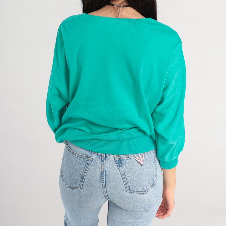 May include: A teal blue long-sleeved sweater with a ribbed neckline and cuffs. The sweater is made of a soft, comfortable fabric and has a relaxed fit.