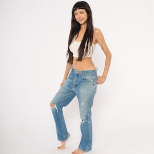 May include: Light blue denim jeans with distressed details, including ripped knees. The jeans have a classic five-pocket design and a relaxed fit. The model is wearing a white crop top.
