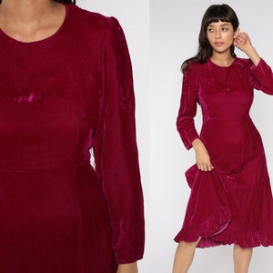 May include: A long-sleeved, magenta velvet dress with a round neckline and a ruffled hem.