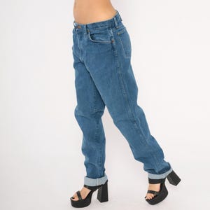 May include: Blue denim jeans with a classic straight leg fit. The jeans have a button and zipper closure, front and back pockets, and are cuffed at the ankles. The model is wearing black platform heels.