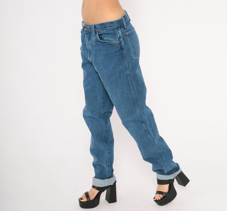 May include: Blue denim jeans with a classic straight leg fit. The jeans have a button and zipper closure, front and back pockets, and are cuffed at the ankles. The model is wearing black platform heels.