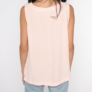 May include: A light pink sleeveless top with a scoop neck. The top is made of a soft, flowing fabric. The back of the top is visible, and the shoulders are slightly wider. The top is a solid color and appears to be a casual style.