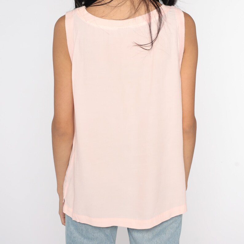 May include: A light pink sleeveless top with a scoop neck. The top is made of a soft, flowing fabric. The back of the top is visible, and the shoulders are slightly wider. The top is a solid color and appears to be a casual style.