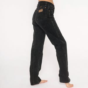 May include: Black denim jeans with a high waist and straight leg. The jeans feature a classic five-pocket design, a brown leather patch on the back, and a button and zip closure. The jeans are worn.