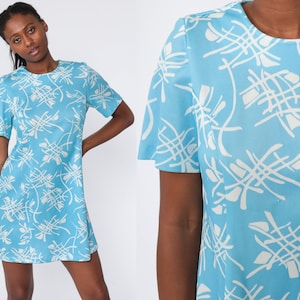 May include: A light blue mini dress with short sleeves and a round neckline. The dress features a white abstract pattern. The dress is made of a lightweight fabric and has a simple, A-line silhouette.