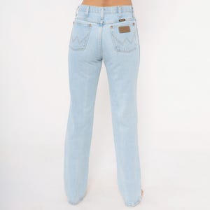 Op de afbeelding: Lichtblauwe denim jeans met een klassiek vijf-zakken ontwerp. De jeans hebben het Wrangler-logo op de achterzak en een bruine leren patch. De jeans hebben een rechte pijp.