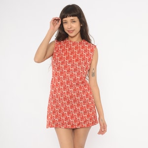 May include: A sleeveless, knee-length dress in a vibrant red hue, adorned with a repeating pattern of beige deer and floral motifs. The dress features a high neckline and a fitted silhouette, showcasing a vintage aesthetic.