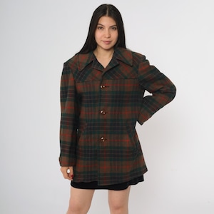 Könnte beinhalten: Eine braune, grüne und rote karierte Jacke mit Kragen und drei braunen Knöpfen. Die Jacke hat lange Ärmel und eine taillierte Passform, geeignet für kühleres Wetter. Das Karomuster ist ein klassisches Design.