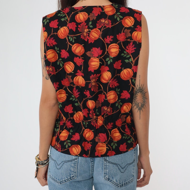 Puede incluir: Una blusa sin mangas con fondo negro y un patr&oacute;n de calabazas naranjas y hojas rojas.