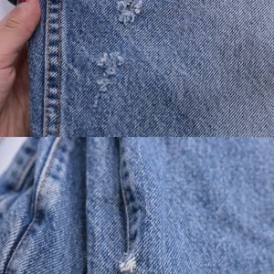 May include: Close-up of light blue denim fabric with several small holes. The fabric is folded and shows the stitching along the edge.