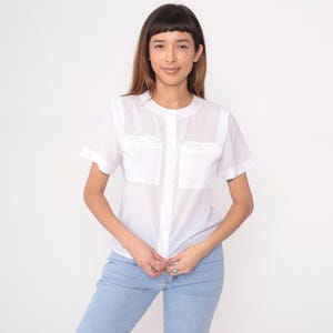 以下が含まれることがあります： 白い半袖シャツ、フロントポケット2つ、ボタン留めデザイン。 シャツは丸襟で、ライトブルーのジーンズと合わせています。 シャツは軽量生地で作られています。