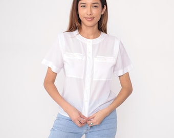May include: White short-sleeve shirt with two front pockets and a button-up design. The shirt has a round collar and is paired with light blue jeans. The shirt is made of a lightweight fabric.