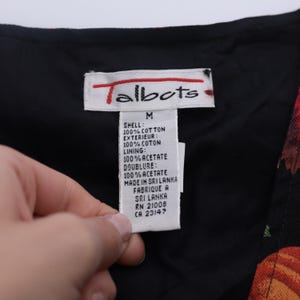 Puede incluir: Una etiqueta de ropa negra de la marca Talbots con texto blanco. La etiqueta indica que el contenido del tejido es 100% algod&oacute;n para la c&aacute;scara y el exterior, y 100% acetato para el forro y la doublure. La etiqueta tambi&eacute;n indica que la prenda se fabric&oacute; en Sri Lanka. La etiqueta incluye la talla M, RN 21008 y CA 23147.