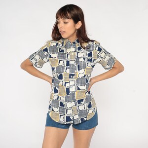 May include: A short-sleeved button-down shirt with a geometric pattern in shades of blue and yellow. The shirt has a collared neckline and a relaxed fit.