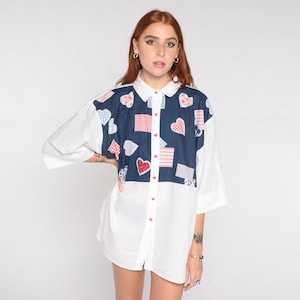 May include: A white button-down shirt with a blue panel featuring a patchwork design of red and white hearts and checkered patterns.