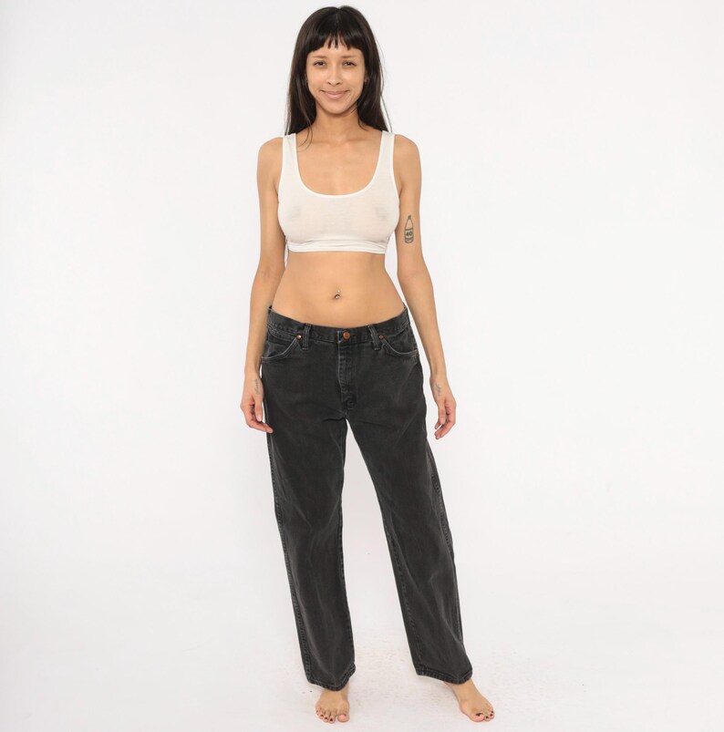 May include: A woman wearing a white crop top and black jeans. The jeans have a button and zipper closure and a relaxed fit. The top is a simple, sleeveless design.