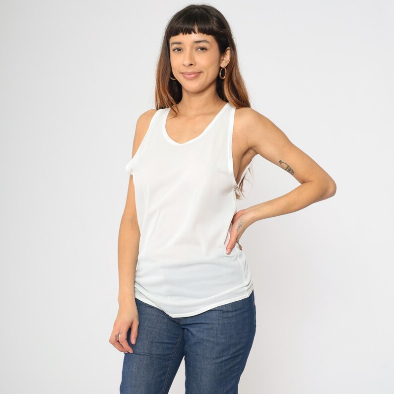 Peut inclure: Un d&eacute;bardeur blanc avec un col rond et une coupe l&eacute;g&egrave;rement ample. Le haut est fait d'une mati&egrave;re l&eacute;g&egrave;re. Le mod&egrave;le porte un jean bleu. Le fond est blanc uni.