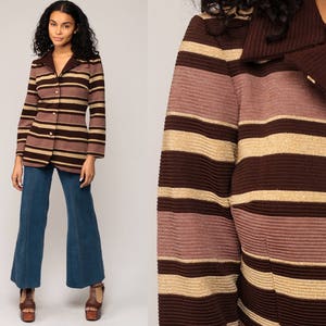 May include: A long-sleeved blazer featuring horizontal stripes in shades of dark brown, light brown, and metallic gold. The garment has a ribbed texture, a solid dark brown collar, and a front button closure. It is paired with blue flared jeans.