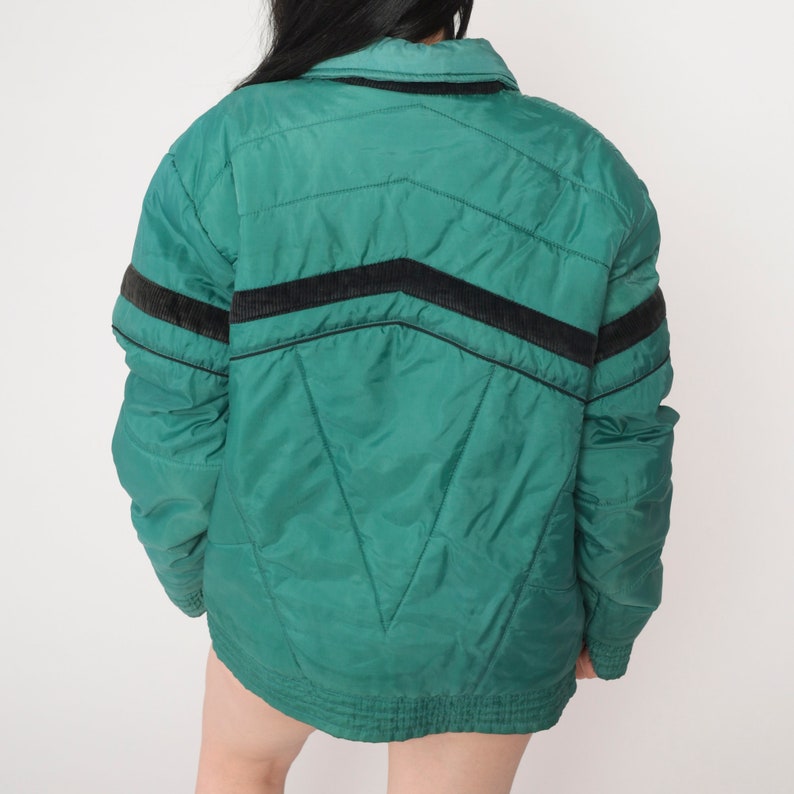 May include: A green quilted jacket with black and brown stripes on the sleeves. The jacket has a zipper closure and a stand-up collar.