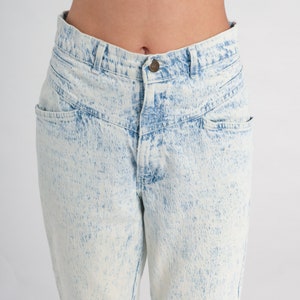 May include: Light blue acid wash denim jeans with a high waist and a relaxed fit.