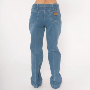 May include: Light blue denim jeans with a classic five-pocket design. The jeans feature a straight leg cut and a brown leather patch on the back pocket with the brand name. The jeans are made of a durable denim material.