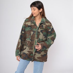 Könnte beinhalten: Eine grüne, braune und schwarze Tarnjacke mit Reißverschluss und einem Aufnäher mit der Aufschrift "U.S. ARMY".