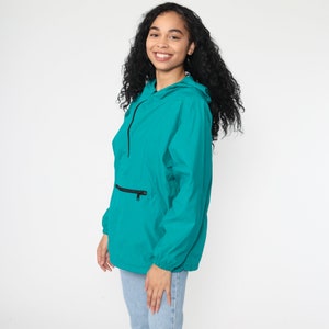 May include: Teal blue hooded jacket with a zipper closure and a front pocket. The jacket has a relaxed fit and is made of a lightweight material.