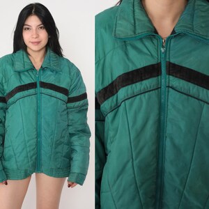 May include: A green quilted jacket with black and brown stripes. The jacket has a zipper closure and a stand-up collar.