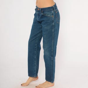 May include: Blue denim jeans with a classic straight-leg fit. The jeans have a button and zipper closure, front and back pockets, and belt loops. The denim is a medium wash with subtle fading and wear.