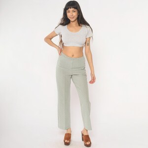 May include: A light gray crop top and light green patterned pants. The pants have a geometric design. The model is wearing brown platform heels. The background is white.