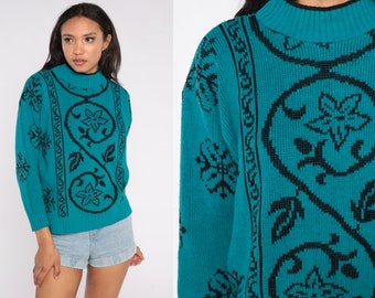 May include: Teal-colored sweater with a black floral pattern. The sweater has a mock turtleneck and long sleeves. The black design includes stylized flowers and vines. The sweater is made of a knitted material.