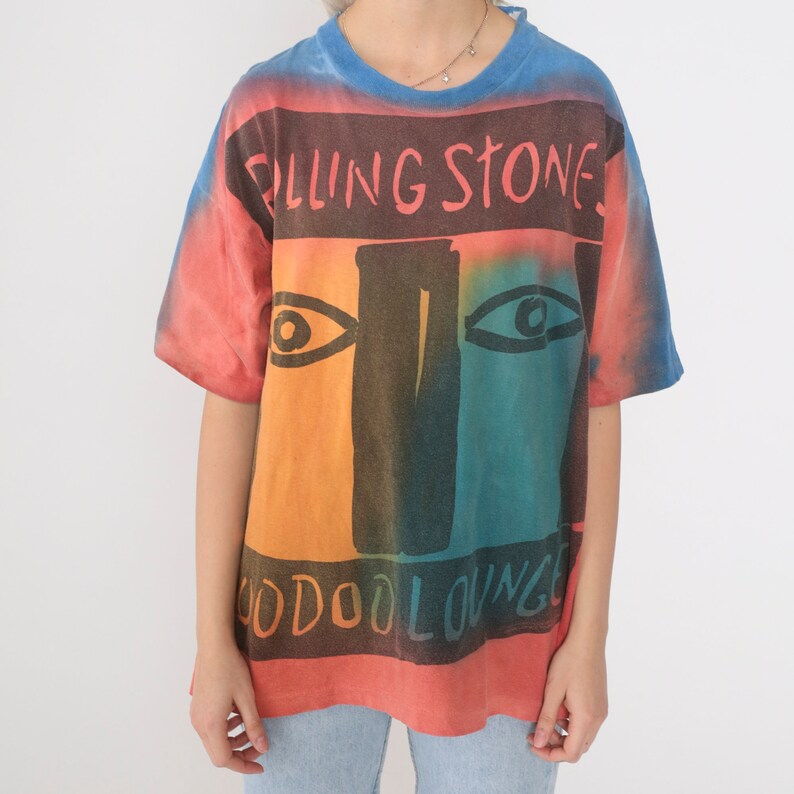 May include: A tie-dye t-shirt with a colorful graphic of a face and the text "Rolling Stones Voodoo Lounge".