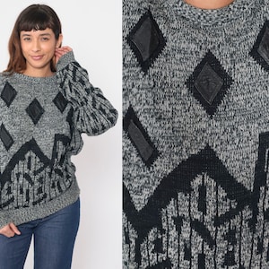 May include: A gray and black sweater with a geometric pattern and black leather accents. The sweater has a crew neck and long sleeves.
