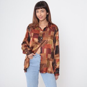 May include: A patterned button-down shirt in shades of brown, orange, and black. The long-sleeved shirt features a patchwork design and a collared neckline. The silky shirt is unbuttoned, revealing a glimpse of the wearer's midriff.