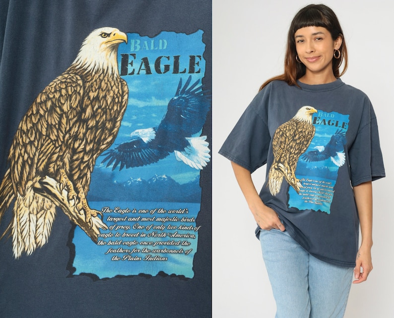 May include: A dark blue t-shirt featuring a graphic print of a bald eagle. The text "BALD EAGLE" is printed in white on the shirt. The shirt also includes a description of the bald eagle, stating that it is one of the world's largest and most majestic birds of prey. The text is printed in white on a blue background.