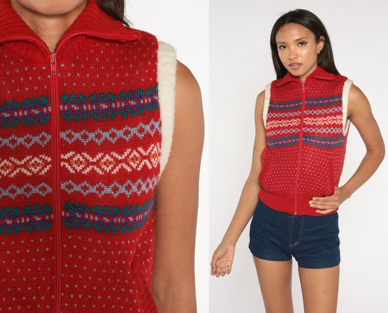 May include: Red knitted waistcoat with a white faux fur collar and a zip fastening. The waistcoat has a geometric pattern in shades of blue, green, and pink.