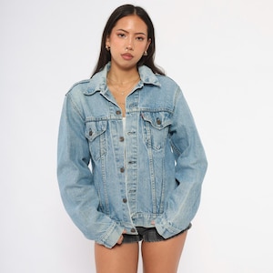 May include: Light blue denim jacket with button closures and chest pockets. The jacket has a classic collar and long sleeves. A vintage style denim jacket.